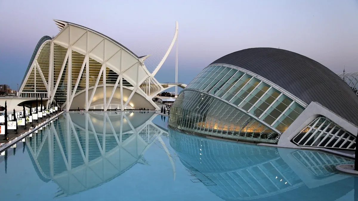 The City of Arts and Sciences in Valencia, Spain, featuring three buildings with unique architectural designs and a large pool of water in front of them.